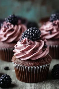 Delicious chocolate cupcakes with blackberry buttercream frosting on a white plate.